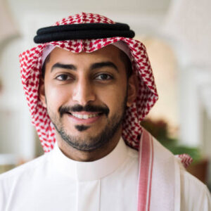 1 (3) Head and shoulder view of Middle Eastern man wearing traditional dish dash, kaffiyeh, and agal and smiling at camera.